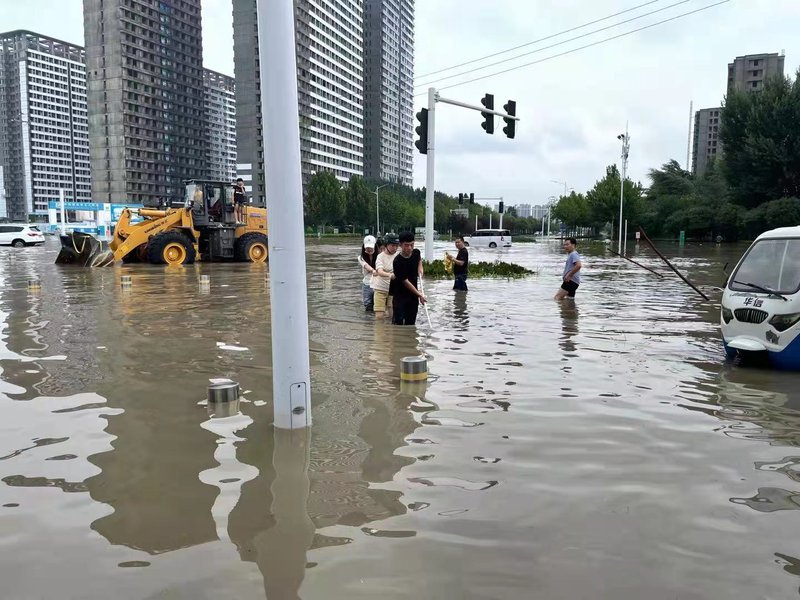 ▲2021年7月21日，在郑州一号线博学路地铁站附近，几位年轻人互相扶助在水中前行。新京报记者 涂重航 摄